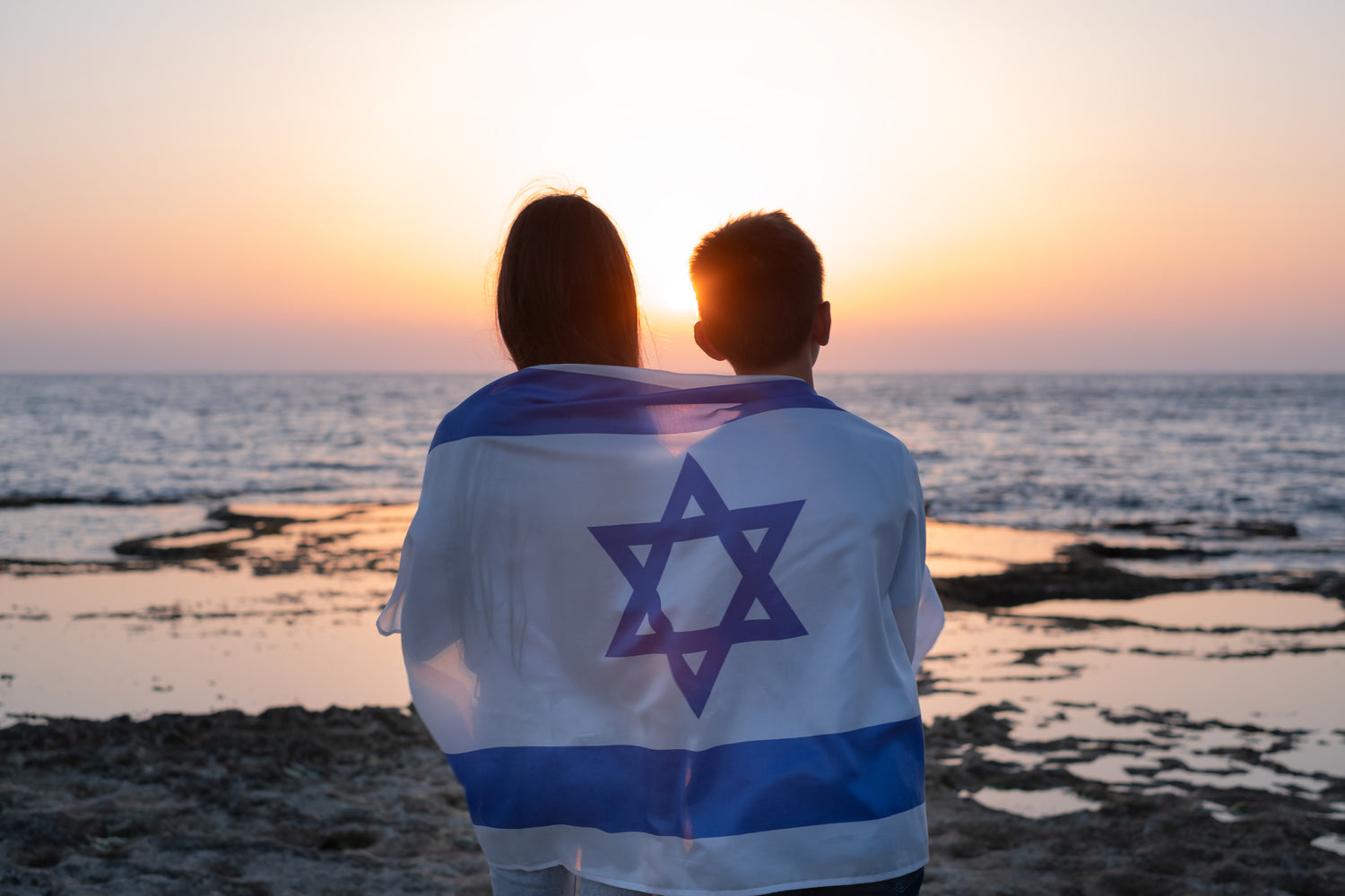 Boy and girl wrapped in the Israeli flag standing together, symbolizing unity and hope.